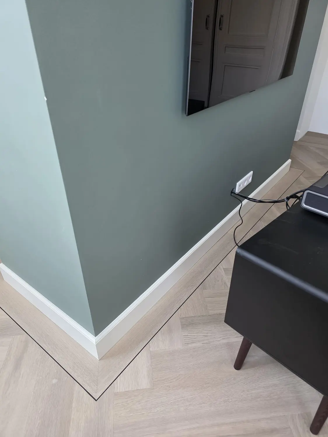 Witte profielplint langs parket en een groene wand